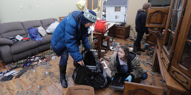 Melinda St. John, left, helps her niece, Jasmin Mueller, 16, lower right, recover valuables from the living room of a house owned by St. John's sister Beth Mueller, Wednesday, Dec. 19, 2018, in Port Orchard, Wash., the day after a tornado took the roof off the house and caused other damage Tuesday. St. John said that no one was at the house during the storm, and that all of the family pets survived. (AP Photo/Ted S. Warren)