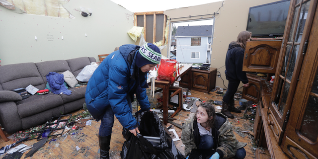 Melinda St. John, left, helps her niece, Jasmin Mueller, 16, lower right, recover valuables from the living room of a house owned by St. John's sister Beth Mueller, Wednesday, Dec. 19, 2018, in Port Orchard, Wash., the day after a tornado took the roof off the house and caused other damage Tuesday. St. John said that no one was at the house during the storm, and that all of the family pets survived. (AP Photo/Ted S. Warren)
