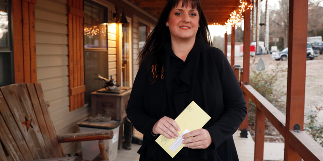 In this Thursday, Dec. 20, 2018 photo, Reagen Adair holds on to a RIP Medical Debt yellow envelope as she poses for a photo at her home in Murchison, Texas. The co-founders of RIP Medical Debt buy millions of dollars in past-due medical debt for pennies on the dollar. But instead of hounding people to pay, they send letters saying the debt is erased, no strings attached. (AP Photo/Tony Gutierrez)