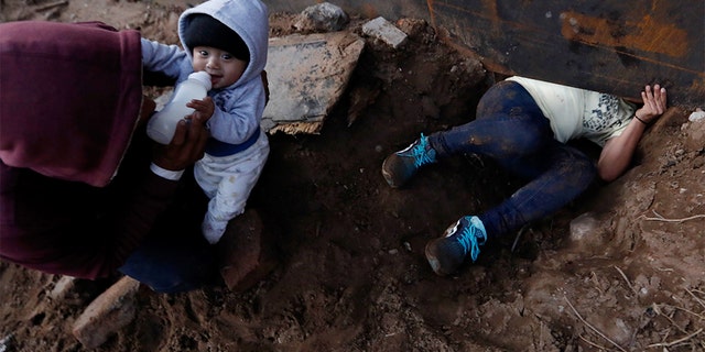Honduran migrant Joel Mendez, 22, feeding his eight-month-old son Daniel as his partner Yesenia Martinez, 24, crawled through the hole under the U.S. border wall. (AP Photo/Rebecca Blackwell)