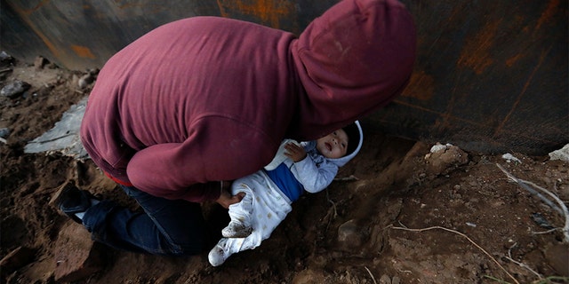 Honduran migrant Joel Mendez, 22, passing his eight-month-old son Daniel through a hole under the U.S. border wall to his partner, Yesenia Martinez, 24, who had already crossed in Tijuana, Mexico, on Friday. (AP Photo/Rebecca Blackwell)