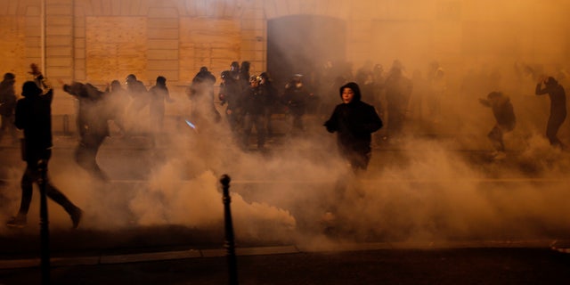 Demonstrators run away to avoid tear gas during clashes Saturday, Dec. 8, 2018 in Paris.