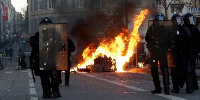 Riot police officer stand in front a burning trash bin during clashes, Saturday, Dec. 8, 2018 in Marseille, southern France.