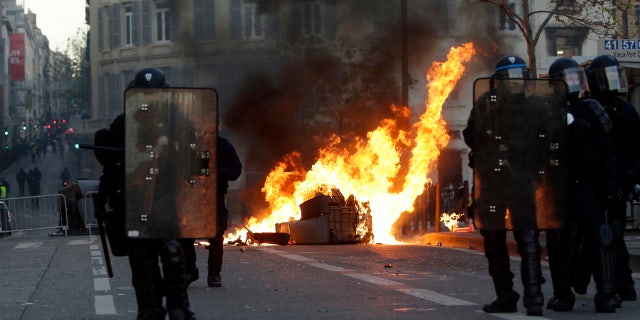 Riot police officer stand in front a burning trash bin during clashes, Saturday, Dec. 8, 2018 in Marseille, southern France.