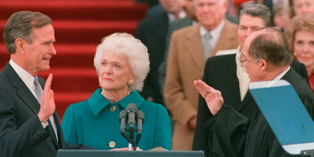 FILE - In this Jan. 20, 1989, file photo, President George H.W. Bush raises his right hand as he is sworn into office as the 41st president of the United States by Chief Justice William Rehnquist outside the west front of the Capitol as first lady Barbara Bush holds the Bible for her husband. Bush died at the age of 94 on Friday, Nov. 30, 2018, about eight months after the death of his wife, Barbara Bush. (AP Photo/Bob Daugherty, File)