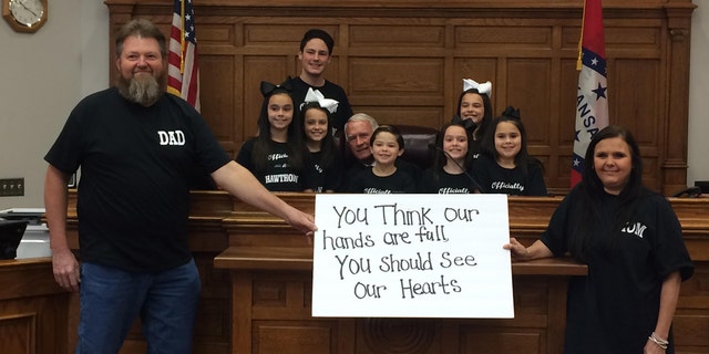 Michael and Terri Hawthorn pose with a sign the day they adopted seven siblings to their family.