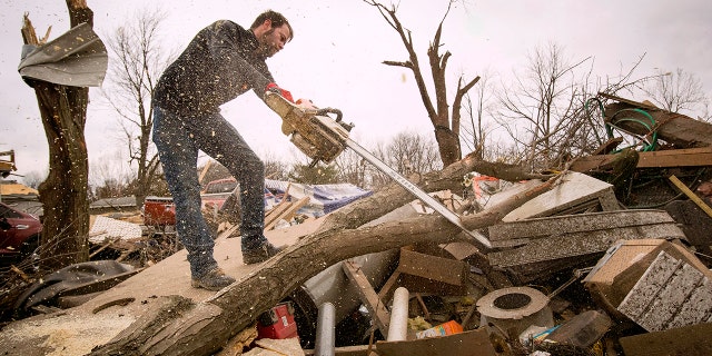 Steven Tirpak using a chainsaw to remove tree branches that fell onto his two-story home in Taylorville, Ill., Sunday. (Ted Schurter/The State Journal-Register via AP)