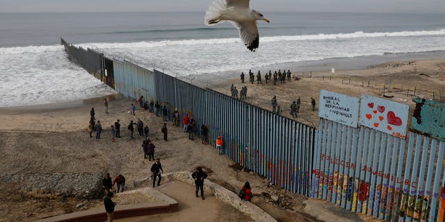 People look on from the Mexican side, left, as U.S. Border Patrol agents on the other side of the U.S. border wall in San Diego prepare for the arrival of hundreds of pro-migration protestors, seen from Tijuana, Mexico, Monday, Dec. 10, 2018. (AP Photo/Rebecca Blackwell)