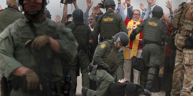 U.S. Border Patrol agents make arrests as they hold a line during a pro-migration protest by members of various faith groups showing support for Central American asylum-seekers who arrived in recent caravans and calling for an end to migrant detentions and deportations, in San Diego as seen through the border fence from Tijuana, Mexico, Monday, Dec. 10, 2018. (AP Photo/Rebecca Blackwell)