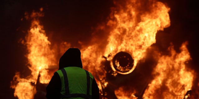 A demonstrator watches a burning car near the Champs-Elysees avenue during a demonstration Saturday in Paris. 