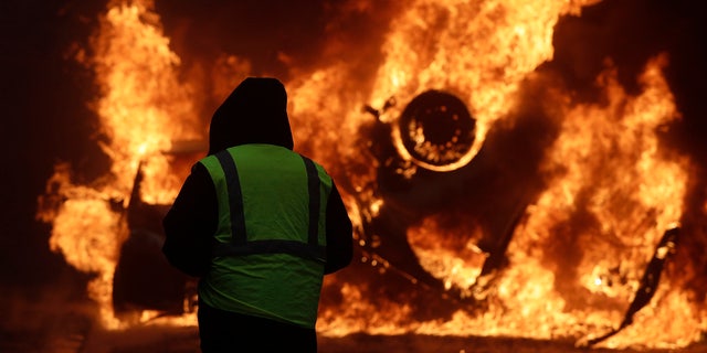 A demonstrator watches a burning car near the Champs-Elysees avenue during a demonstration Saturday in Paris.