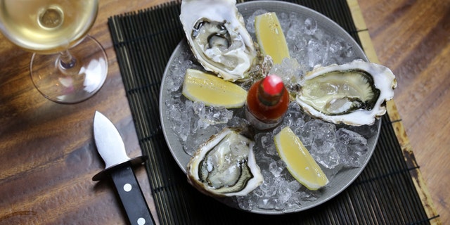 Overhead photo of oysters with wine and copy space. Served on ice with tabasco sauce. Well presented on a wooden table.