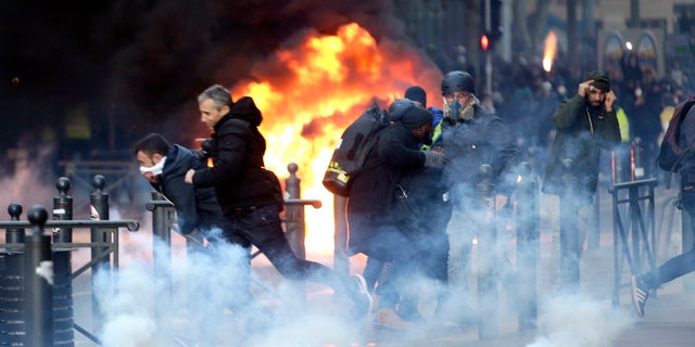 People run away from a burning car during clashes, Saturday, Dec. 8, 2018 in Marseille, southern France. (AP Photo/Claude Paris)