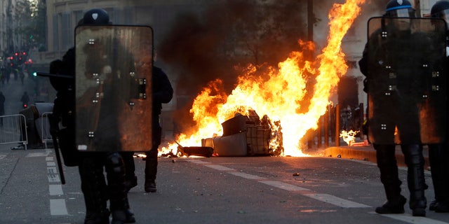 Riot police officers stand in front a burning trash bin during clashes, Saturday, Dec. 8, 2018 in Marseille, southern France. 