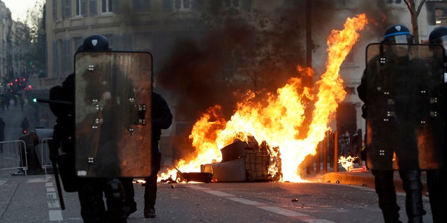 Riot police officers stand in front a burning trash bin during clashes, Saturday, Dec. 8, 2018 in Marseille, southern France. 