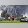 People play golf as an ash plume rises in the distance from the Kilauea volcano on Hawaii's Big Island, May 15, 2018. 