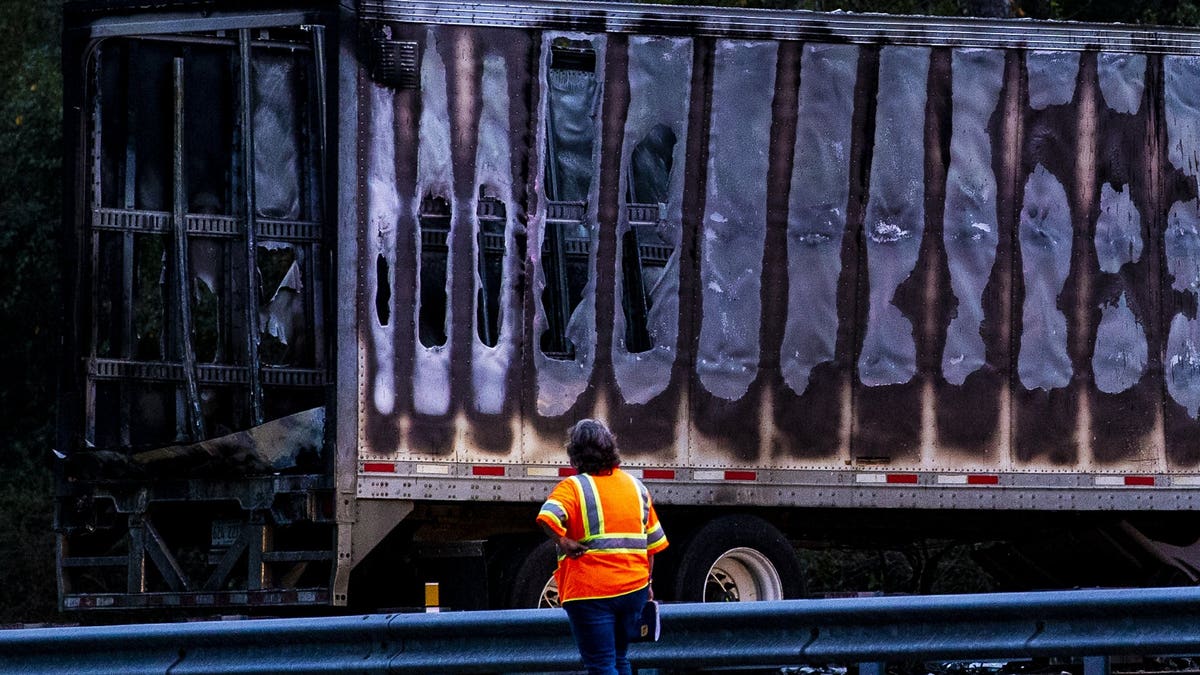 A worker looks at a charred semi-truck after a wreck with multiple fatalities on Interstate 75, south of Alachua, near Gainesville, Fa., Thursday, Jan. 3, 2019. Two big rigs and two passenger vehicles collided and spilled diesel fuel across the Florida highway Thursday, sparking a massive fire that killed several people, authorities said.