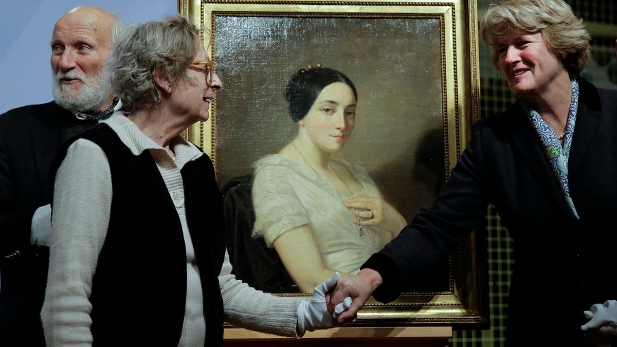 Government Commissioner for Culture and the Media Monika Gruetters, right, overhands the painting 'Portrait of a Seated Young Woman' by Thomas Couture to Franz Rainer Wolfgang Joachim Kleinertz, left, and Maria de las Mercedes Estrada, second from left, heirs of Jewish French politician Georges Mandel, during a restitution ceremony in Berlin. (AP Photo/Markus Schreiber)