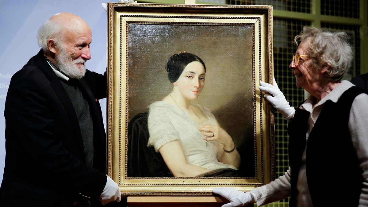 Franz Rainer Wolfgang Joachim Kleinertz, left, and Maria de las Mercedes Estrada, right, heirs of Jewish French politician Georges Mandel stand next to the painting 'Portrait of a Seated Young Woman' by Thomas Couture during a restitution ceremony in Berlin. (AP Photo/Markus Schreiber)