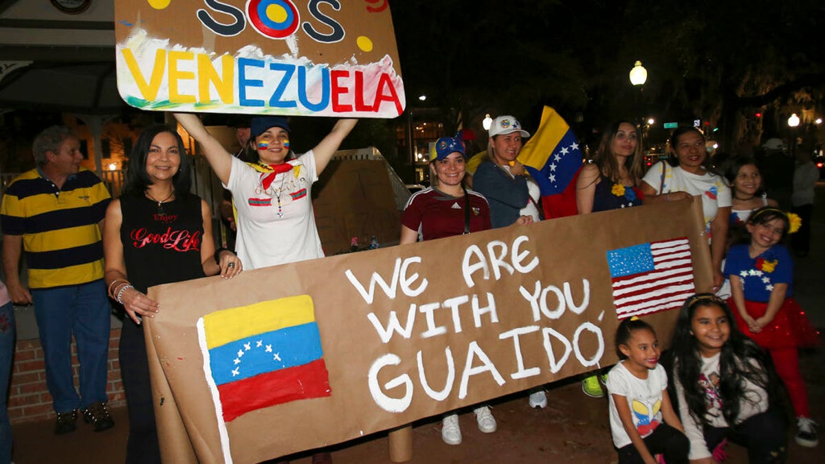 People hold signs and pose for pictures as they protest against Venezuelan President Nicolas Maduro with about 150 other people on the Ocala Downtown Square in Ocala, Fla., Wednesday, Jan. 23, 2019. The protestors in Ocala joined thousands of Venezuelans who took to the streets in Caracas, Venezuela, Wednesday, answering the opposition's call for a nationwide protest to rid Maduro from the office. (Bruce Ackerman/Star-Banner via AP)