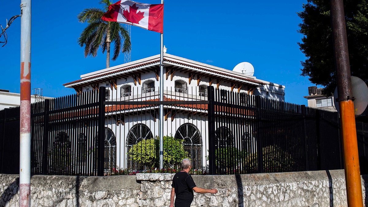 FILE - In this April 17, 2018 file photo, a man walks beside Canada's embassy in Havana, Cuba. Canada announced Wednesday, Jan. 30, 2019, it is removing up to half of the Canadians at its embassy in Cuba after another diplomat was found to have fallen mysteriously ill. Canada has confirmed 14 cases of mysterious health problems since early 2017. (AP Photo/Desmond Boylan, File)