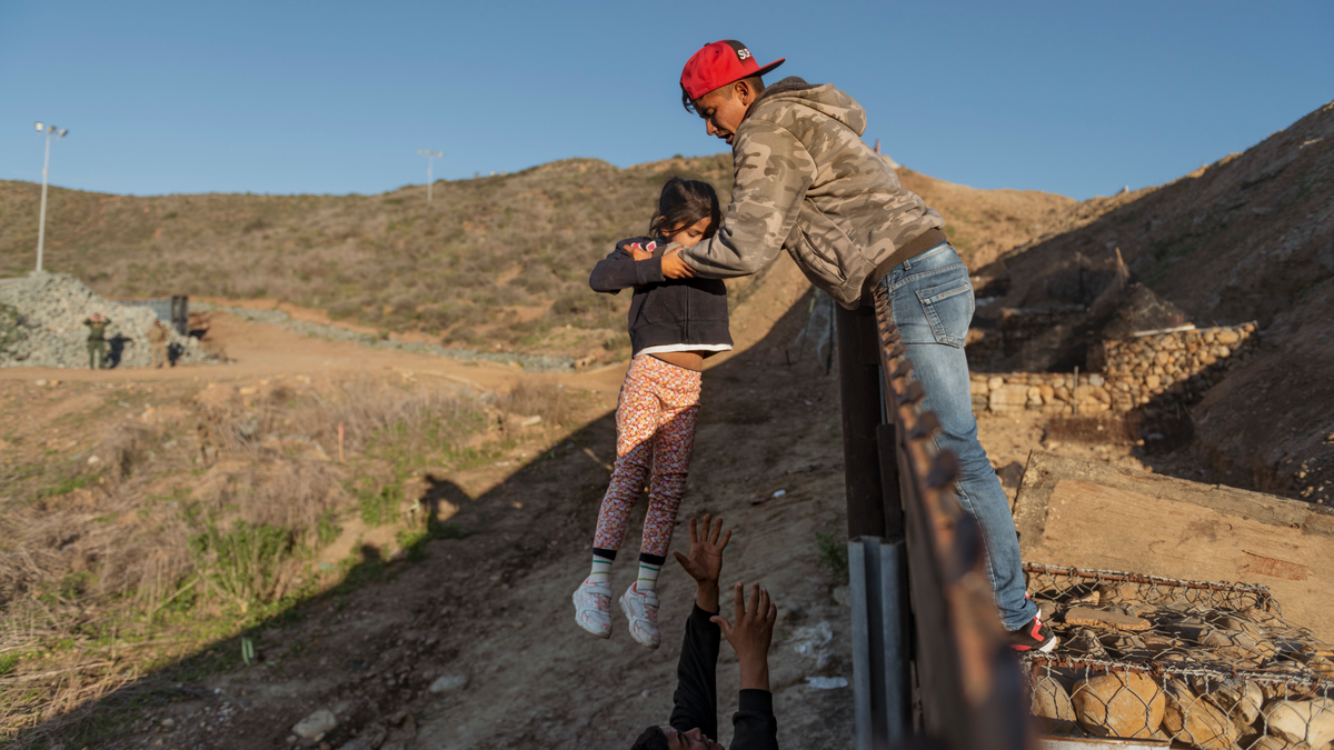 Jan 3: A migrant from Honduras pass a child to her father after he jumped the border fence to get into the U.S. side to San Diego, Calif., from Tijuana (AP Photo/Daniel Ochoa de Olza)