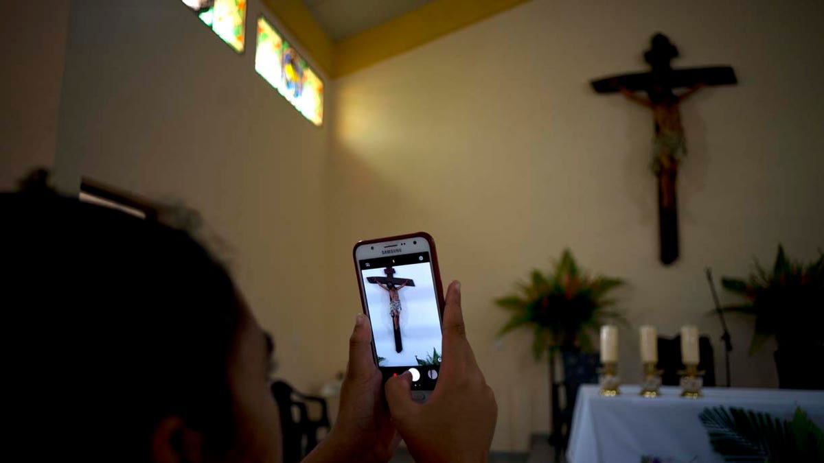 A parishioner makes a photo of the crucifix above the altar at the newly consecrated Sagrado Corazon de Jesus, or Sacred Heart, Catholic church, in Sandino, Cuba, Saturday, Jan. 26, 2019. (AP Photo/Ramon Espinosa)