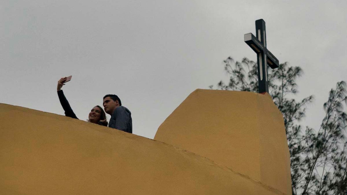 A couple pose for a photo backdropped by the cross crowning the newly consecrated Sagrado Corazon de Jesus Catholic church or Sacred Heart, in Sandino, Cuba, Saturday, Jan. 26, 2019. (AP Photo/Ramon Espinosa)