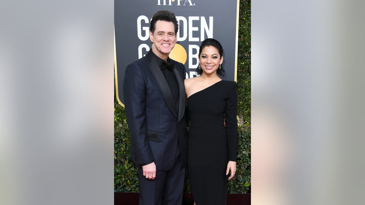 Jim Carrey, in a navy blue tux, and girlfriend Ginger Gonzaga, in a one shoulder dress, keep close on the red carpet.