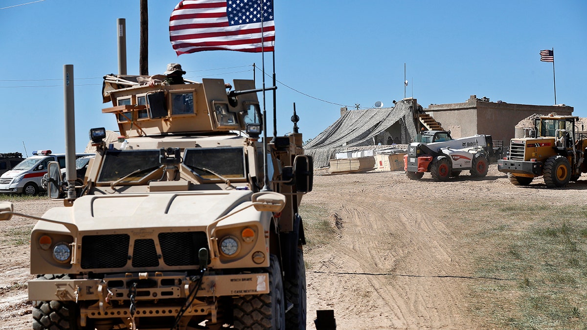 A large military vehicle with a US flag drives away from a US base in Syria