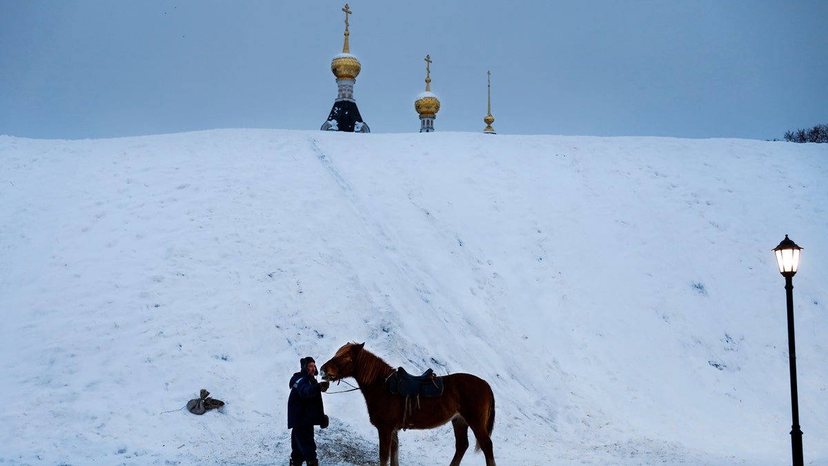 A man prepares a horse to ride tourists during a cold winter day at a hill, near the Assumption Cathedral in the small Russian town of Dmitrov.