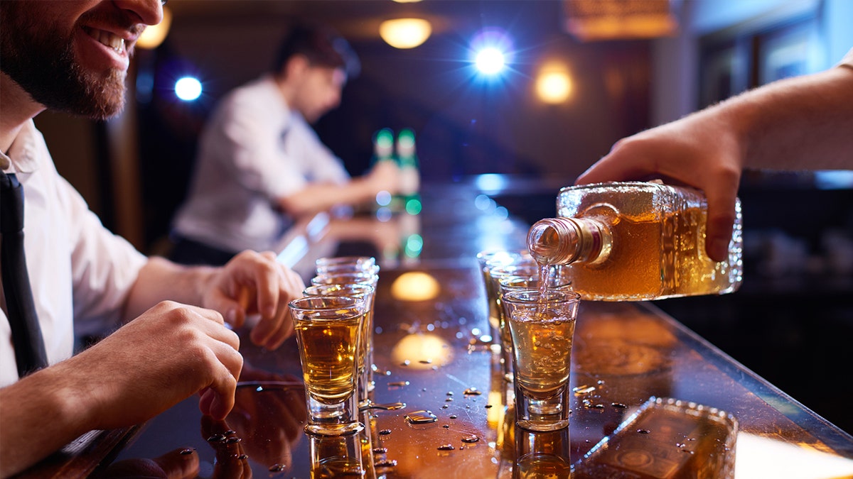 Bartender pouring shots of liquor as customer sits across smiling