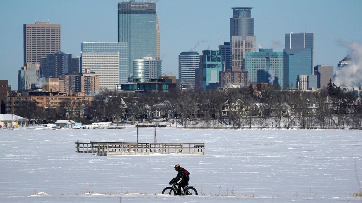 A cyclist decked out in cold weather gear rides past the city skyline and a frozen Bde Maka Ska in Minneapolis. (Anthony Souffle/Star Tribune via AP)