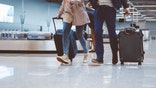 Low angle view of people in international airport walking with luggage. Couple at airport terminal with suitcase.