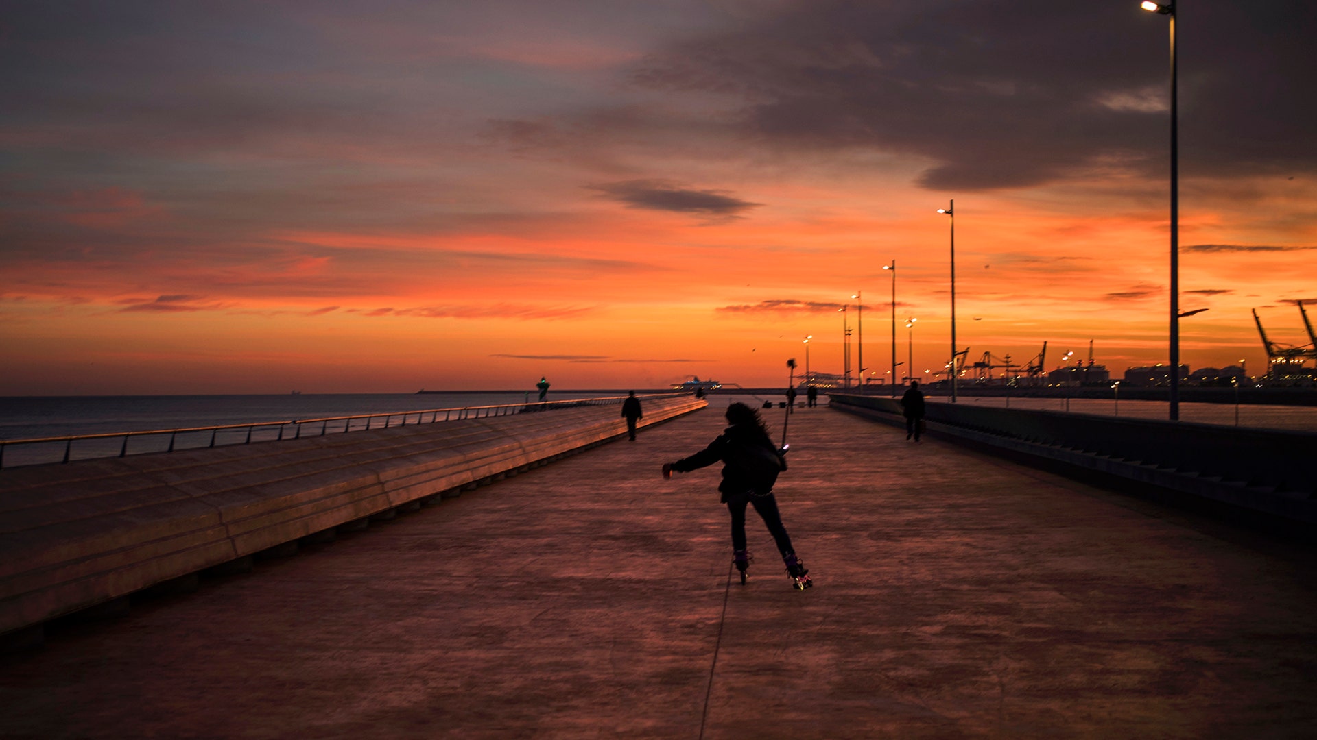 A woman skates along a promenade facing the mediterranean sea, as the sun sets at the port of Barcelona, Spain, Jan. 8, 2019.