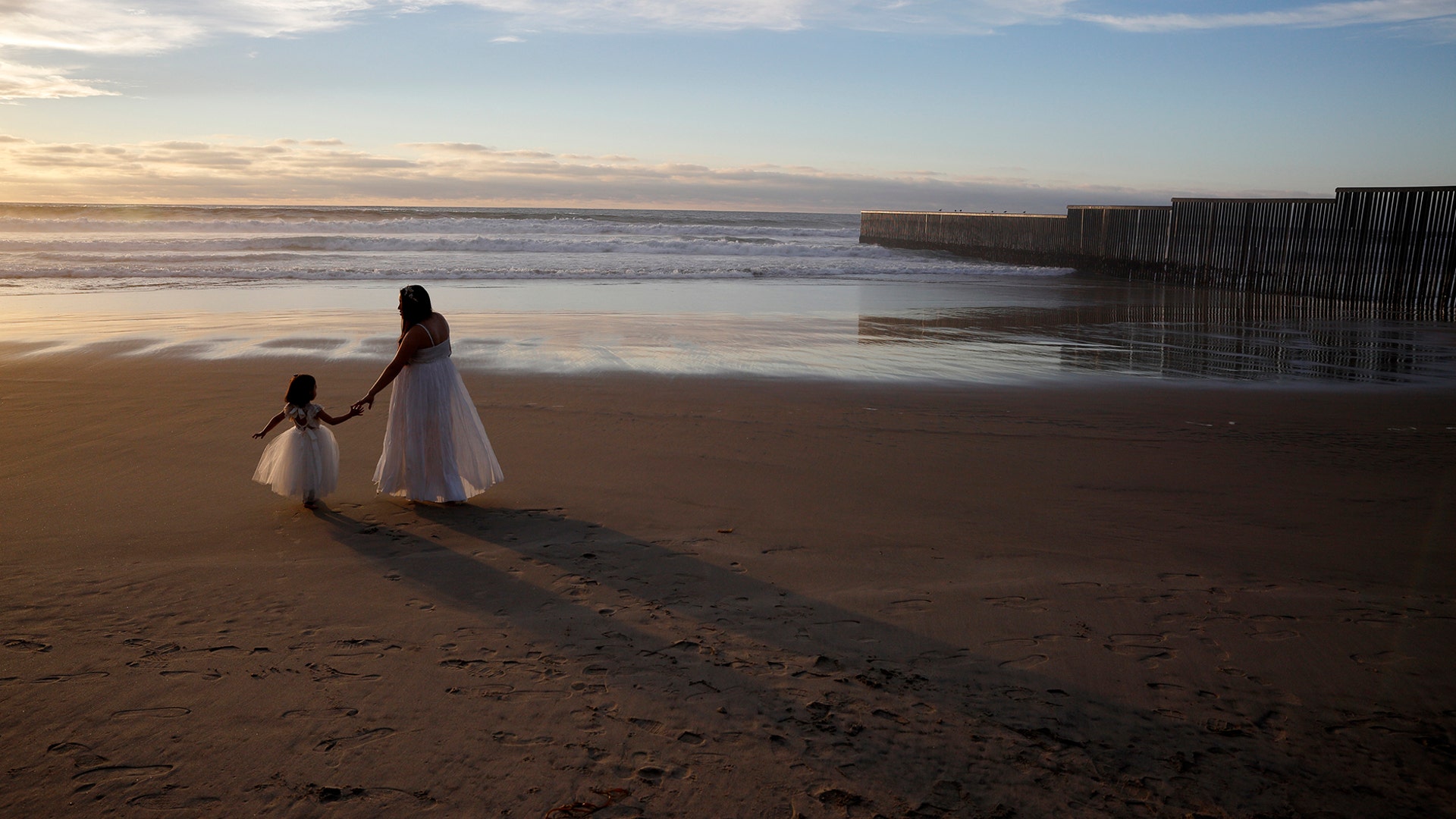Ileze Dariel, of Tijuana, Mexico, reaches for the hand of her daughter, Jimena, as they wait for a photographer while taking family pictures on the beach next to the border wall in Tijuana, Mexico, Jan. 9, 2019. 