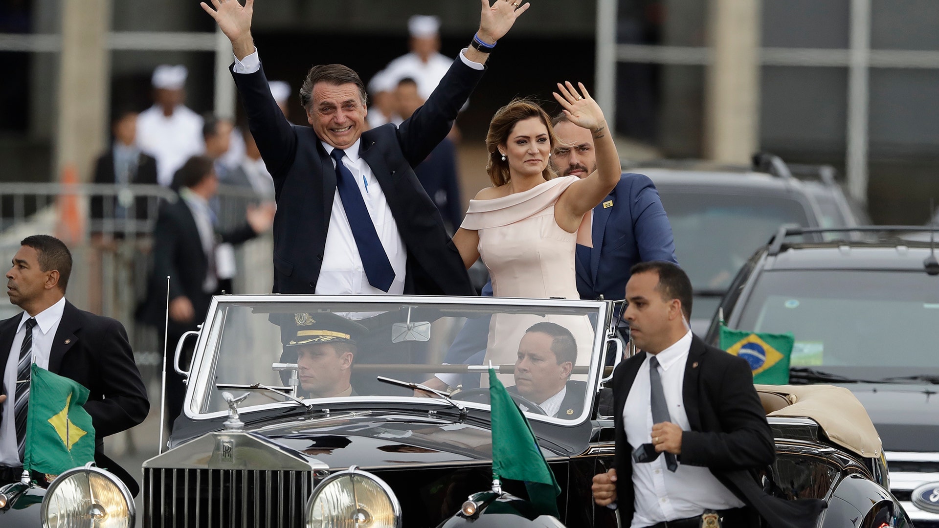 Flanked by first lady Michelle Bolsonaro, Brazil's President Jair Bolsonaro waves as he rides in an open car after his swearing-in ceremony, in Brasilia, Brazil, Jan. 1, 2019. 