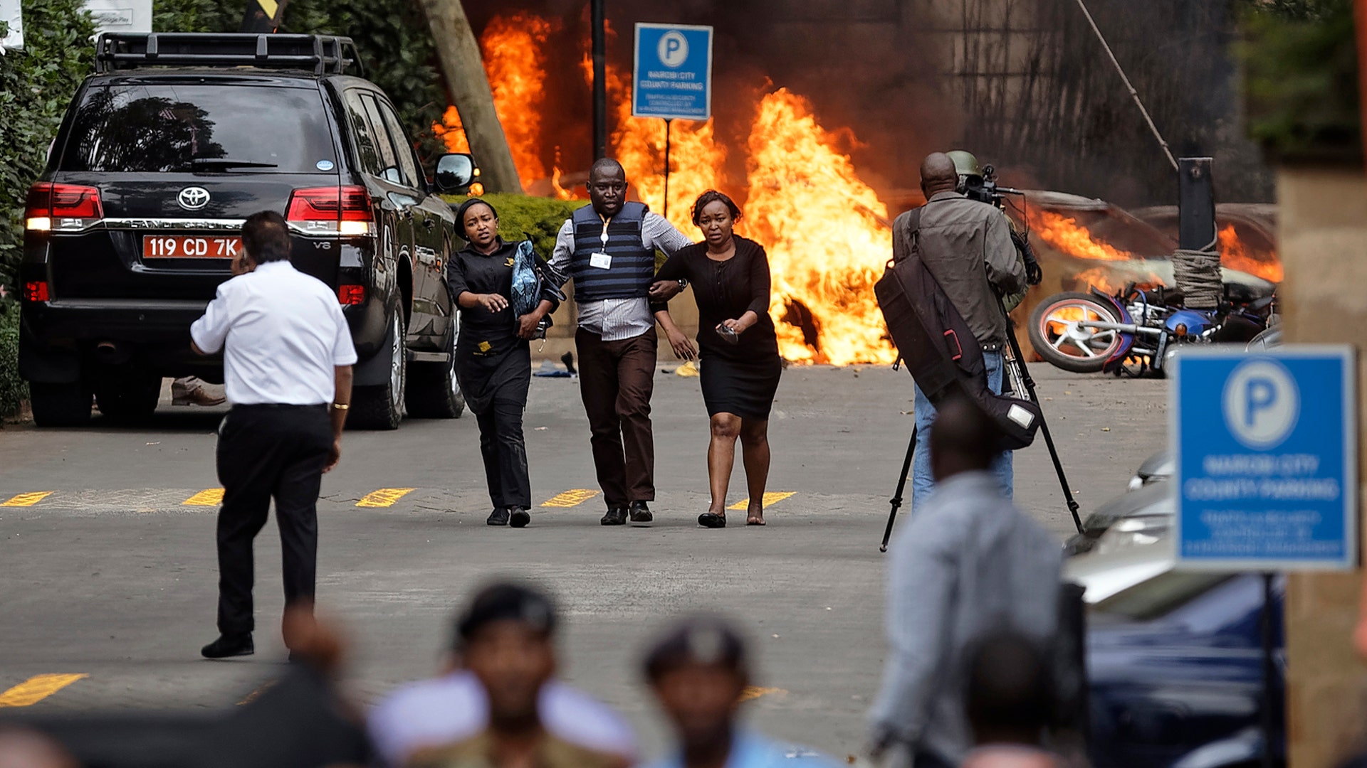 Security forces help civilians flee the scene of a bombing as cars burn at a hotel complex in Nairobi, Kenya, Jan. 15, 2019. 