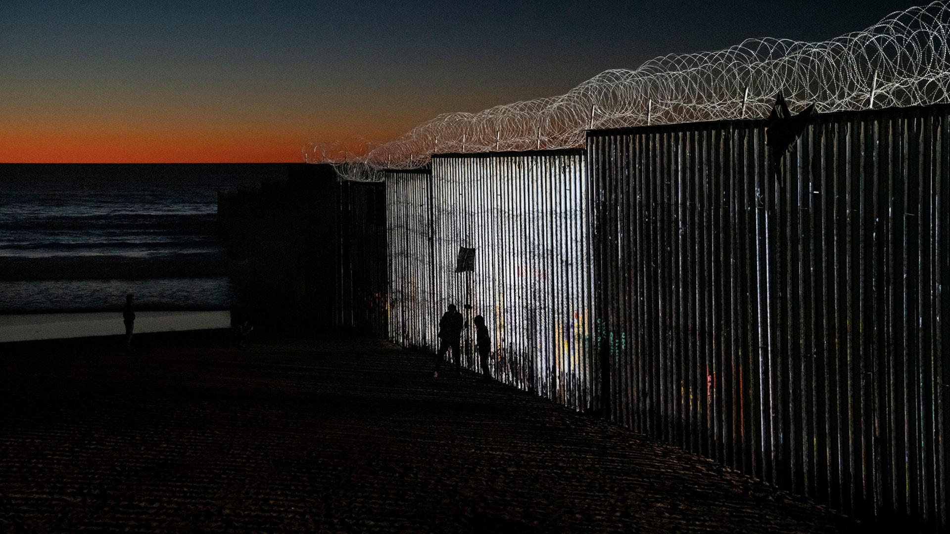 The sun sets while people walk next to the border fence between the U.S. side of San Diego and Tijuana, in Mexico, Jan. 2, 2019. 