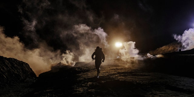 Migrants running as U.S. Border Protection officers threw tear gas to the Mexican side of the border fence on Jan. 1, 2019. (AP Photo/Daniel Ochoa de Olza)