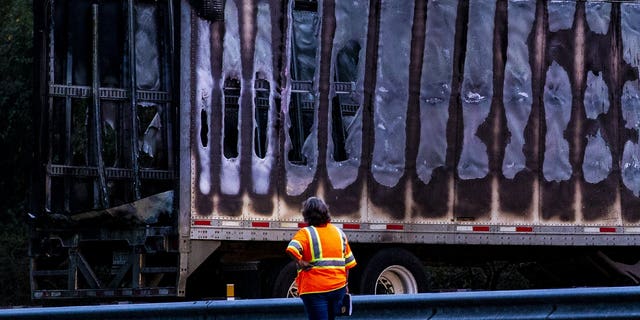 A worker looks at a charred semi-truck after a wreck with multiple fatalities on Interstate 75, south of Alachua, near Gainesville, Fa., Thursday, Jan. 3, 2019. Two big rigs and two passenger vehicles collided and spilled diesel fuel across the Florida highway Thursday, sparking a massive fire that killed several people, authorities said.