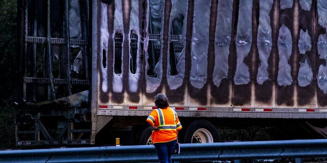 A worker looks at a charred semi-truck after a wreck with multiple fatalities on Interstate 75, south of Alachua, near Gainesville, Fa., Thursday, Jan. 3, 2019. Two big rigs and two passenger vehicles collided and spilled diesel fuel across the Florida highway Thursday, sparking a massive fire that killed several people, authorities said.