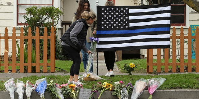 Sydney Carlier, foreground, accompanied by roommates, Jenna Brouwer, center and Camille Foder, behind flag, places flowers on a memorial for slain Davis Police Officer Natalie Corona, on Friday in Davis, Calif.