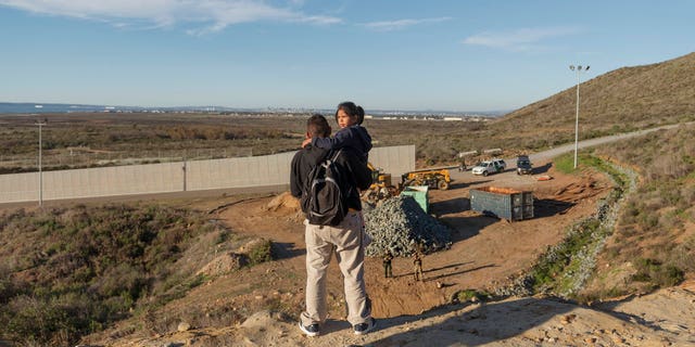 A migrant from Honduras holds his daughter while Border Patrol Officers look at them before they jump the border fence to get into the U.S. side to San Diego, Calif., from Tijuana, Mexico, Thursday, Jan. 3, 2019. Discouraged by the long wait to apply for asylum through official ports of entry, many migrants from recent caravans are choosing to cross the U.S. border wall and hand themselves in to border patrol agents. (AP Photo/Daniel Ochoa de Olza)