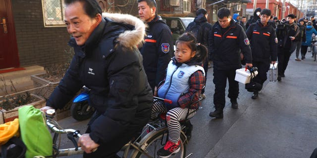 A man rides with a student past crime scene investigators as they leave the Beijing No. 1 Affiliated Elementary School of Xuanwu Normal School in Beijing, China, Tuesday, Jan. 8, 2019.