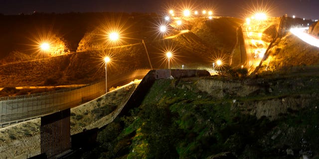 FILE - In this Monday, Jan. 7, 2019, file photo, floodlights from the U.S, illuminate multiple border walls, seen from Tijuana, Mexico. (AP Photo/Gregory Bull, File)