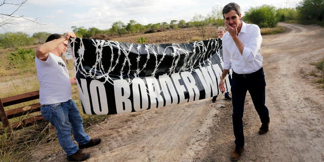 FILE - In this Saturday, Jan. 6, 2018, file photo, Texas Democratic Congressman Beto O'Rourke, right, passes a "No Border Wall" sign during a visit to the National Butterfly Center in Mission, Texas, a possible location for a border wall. President Donald Trump is not giving up on his demands for $5.7 billion to build a wall along the U.S.-Mexico border, saying a physical barrier is central to any strategy for addressing the security and humanitarian crisis at the southern border. Democrats argue that funding the construction of a steel barrier along roughly 234 miles will not solve the problems. (AP Photo/Eric Gay, File)