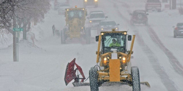 Motor graders plow Rosser Avenue as snow falls, Friday, Jan. 18, 2019, in Bismarck, N.D.