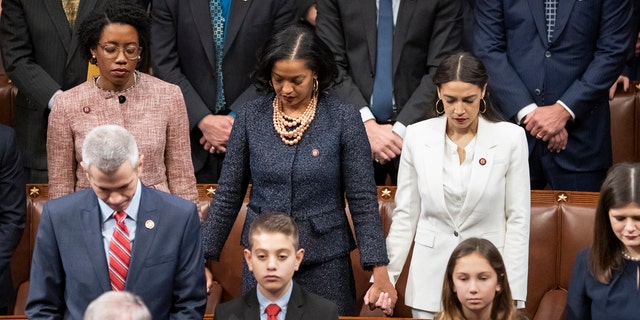 From left in center row, Rep. Lauren Underwood, D-Ill., Rep. Jahana Hayes, D-Conn., and Rep. Alexandria Ocasio-Cortez, D-N.Y, hold hands during an opening prayer as the House of Representatives assembles for the first day of the 116th Congress at the Capitol in Washington, Thursday, Jan. 3, 2019. (AP Photo/J. Scott Applewhite)