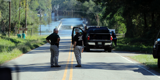 FILE - In this Wednesday, Sept. 19, 2018, file photo, responders congregate near where two people drowned the evening before when they were trapped in a Horry County Sheriff's transport van while crossing an overtopped bridge over the Little Pee Dee River on Highway 76, during rising floodwaters in the aftermath of Hurricane Florence in Marion County, S.C. Charges are expected to be filed Friday, Jan. 4, 2019, against two South Carolina law enforcement officers who were transporting two mental patients who drowned while locked in the back of a van during the hurricane. (AP Photo/Gerald Herbert, File)